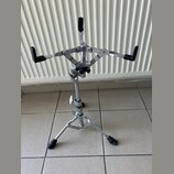 Kovový stojan na hudební nástroj s chromovaným povrchem a černými gumovými koncovkami. Stojan má tříramennou horní část s nastavitelníma rameny a tro…