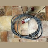Šedý silový kabel smouseDowným červeným konektorem a zásuvkou. Na bílém plastovém krytu konektoru jsou nečitelné nápisy. Kabel je svázaný černými pla…
