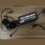 Černý obdélníkový zdroj napájení s několika připojenými kabely a konektory. Na horní straně je bílý nápis MULTI POWER SUPPLY a pod ním text SEPARATE…