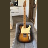 Elektrická kytara s tónem sunburst, krčkem a hmatníkem z přírodního dřeva. Na hlavě je viditelné logo Fender. Kytara má krémový pickguard a chromovan…