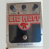 Stříbrný efekt pedál s černým panelem a červenými prvky. Na horní části jsou tři černé oválné ovladače s nápisy AMPLIFIER VOLUME, TONE a INPUT SUSTAI…