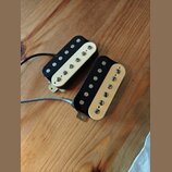 Dvě elektrické kytarové snímače typu humbucker s černým tělem a krémovými plastovými kryty. Snímače jsou vybaveny šesti viditelnými poladovacími šrou…