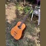 Akustická kytara s přirozenou dřevěnou barvou korpusu a tmavým hnedým hmatníkem. Na hlavě nástroje je viditelný nápis "Cort". Povrch instrumentu vyka…