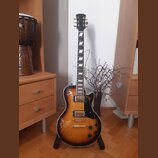 Elektrická kytara s tvarem singlecut a barevným přechodem od žluté k tmavě hnědé (sunburst). Na hlavě je viditelné logo Epiphone. Nástroj má dva humb…