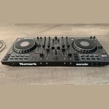 Černý DJ kontrolér s dvěma jog-koly a centrálním mixážním sekcí. Na přístroji jsou viditelné nápisy Numark, serato a modelové označení NS4 FX. V horn…