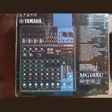 Fotografie zobrazuje míchací pult Yamaha MG10XU v původním kartónovém obalu. Na přístroji je viditelné logo YAMAHA a označení modelu MIXING CONSOLE M…
