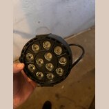 Černý kulatý LED reflektor s 12 světelnými zdroji rozmístěnými v kruhu. Zařízení má plastové tělo a integrovanou úchytnou rukojeť. Na fotce nejsou vi…