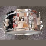Chromovaný malý buben s kovovým korpusem. Uprostřed je černý štítek s bílým nápisem MAPEX PERCUSSION TECHNOLOGY a pod ním menší text MADE IN TAIWAN R…