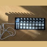 Černý MIDI kontrolér s bílými podsvícenými tlačítky a šeradou otočných knoflíků. Na levé straně je bílý nápis ARTURIA a pod ním text YOUR EXPERIENCE…