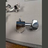 Detailní pohled na jeden chromovaný ladicí kolík kytary. Na kulaté části s nápisem je viditelné logo Jackson®. Povrch vykazuje drobné škrábance a zná…