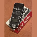 Fotografie zachycuje spodní stranu efekt pedálu v černé barvě s kovovým tělem. Na povrchu jsou nápisy „cry baby“, „MODEL GCB95“ a logo „Dunlop“. Je z…