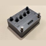 Kompaktní kytarový efekt v šedém kovovém provedení. Na horní straně jsou umístěny ovládací knoflíky s popisky GAIN, BASS, MID, TREBLE a AMOUNT, někol…