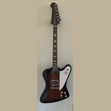 Elektrická kytara s tmavě hnědým gradientním lakem a bílým plechtrátem. Na hlavě je zlatý nápis Epiphone a na plechtrátu se nachází červené logo. Nás…