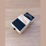 Bílý kytarový pedál s černým spínacím tlačítkem, na kterém je vyražen nápis BOSS. Na horní části je červeným a černým textem uvedeno Chromatic Tuner…