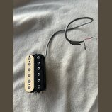 Kytarový snímač s černým plastovým rámečkem a krémově bílým krytem s šesti viditelnými póly. Ze snímače vede šedý kabel s odkrytými červeným a černým…