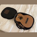 Akustická kytara v dřevěném provedení umístěná v černém měkkém pouzdře. Na hmatníku je viditelný nápis "Fender". Povrch nástroje i pouzdra vypadá čis…