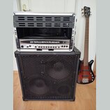 Fotografie zobrazuje basovou kytaru, basový kombozesilovač a rackové pouzdro. Na hlavě kytary je nápis Gallien-Krueger, tělo má červenohnatý sunburst…