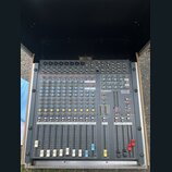 Šedý mixážní pult umístěný v transportním kufru. Na přístroji je vidět bílý nápis ALLEN&HEATH a označení modelu PA12-CP CONSTANT POWER. Povrch pultu…