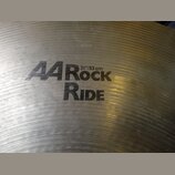 Detailní pohled na kovový činel s viditelným broušením povrchu. Na čineli je černý nápis „A4 Rock RIDE“ a pod ním označení velikosti „21"/53 cm“. Ve…