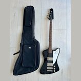 Černá elektrická basová kytara s bílým plechtrátorem a hnědým hmatníkem. Na hlavě nástroje je svisle napsáno logo "Rickenbacker". Vedle kytary leží č…