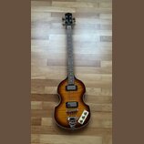 Čtyřstrunná basová kytara s tělem ve tvaru houslí a barevným přechodem od žluté k tmavě hnědé. Na hlavě je viditelné logo Epiphone. Nástroj má dva sn…
