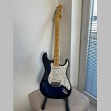 Elektrická kytara s tmavě modrým přechodovým lakem a bílým perleťovým pickguardem. Na hlavě hmatníku je viditelné logo Squier. Krk a hmatník jsou vyr…