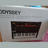 Fotografie zachycuje kartonovou krabici s obrázkem analogového syntetizátoru. Na krabici je velký nápis ODYSSEY a text Analog Synthesizer with 37 Ful…