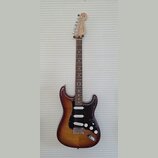 Elektrická kytara s trupem v hnědém sunburst provedení a černým pickguardem. Na hlavě hmatníku je viditelné logo "Squier". Nástroj má tři snímače typ…