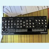 Černý analogový syntetizátor s nápisem SE-02 STUDIO ELECTRONICS a logem Roland. Přední panel obsahuje numeroustočítka, přepínače a sekci s klávesovým…