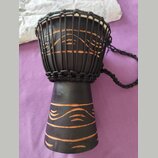 Černý djembe s bílou membránou, nataženou pomocí černých provázků. Tělo nástroje je zdobeno vyrytými vodorovnými a vlnitými liniemi, které odhalují h…
