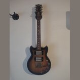 Elektrická kytara s tmavě hnědým gradientem (sunburst) a hnedým hmatníkem. Na hlavě je viditelné logo Epiphone. Nástroj má dva humbuckery, tři ovláda…
