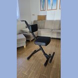 Na fotografii je černá polstrovaná židle s opěradlem a opěrkou pro nohy. Konstrukce je vyvedena v černé barvě, pravděpodobně z kovu. Na předmětu nejs…