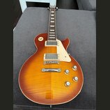Elektrická kytara s trupem v barvě sunburst a viditnou strukturou dřeva. Nástroj má dva humbuckery, bílý plechtrpáč a čtyři zlaté ovládací knoflíky.…