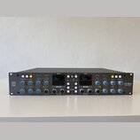 Šedý rackový studiový kompresor s nápisy Solid State Logic vlevo a THE BUS+ vpravo. Přední panel obsahuje dva analogové VU metry, řadu regulačních kn…