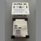 Fotografie zobrazuje stříbrnou kovovou pasivní DI box s černými plastovými zátlačkami na koncích. Na horní straně je nápis DAP AUDIO a model PDI-100…