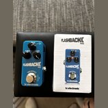 Modrý efekt pedál s nápisy FLASHBACK MINI a tc electronic. Na horní části jsou tři černé oválové knoflíky s popisky DELAY, F. BACK a LEVEL. Ve spodní…