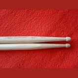 Dvě dřevěné bubnové paličky v přírodní barvě položené na červeném textilním povrchu. Na fotce jsou vidět pouze konce paliček s kulatými hlavami. Žádn…
