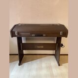 Hnědý klavír nebo digitální piano v dřevěném korpusu s uzavíracím víkem. Na přední spodní části je zlatý nápis „FAKFISA“ s doprovodným logem. Nástroj…