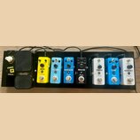 Sada efektů na černém pedalboardu. Zleva jsou vidět pedály s nápisy: SONIC IR (SONICCAKE), VOLWAH, DELAY (Rowin), AC STAGE (Rowin), HARMONIZER (Rowin…