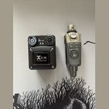 Na fotografii jsou dvě části bezdrátového systému v černé a stříbrné barvě. Levé zařízení má nápis Xvive U4 RECEIVER a dvě otočné kontrolní knoflíky.…