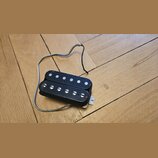 Černý humbucker s dvěma řadami bílých magnetických pólců. Nástroj nemá žádné viditelné značky ani nápisy. K pickupu vede stříbrně opletený kabel.