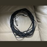 Černý kabel s kovovými konektory na obou koncích. Kabel je svinutý do kruhu a položený na světlém koženém povrchu. Na konektorech nejsou viditelné žá…