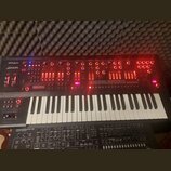 Černý klávesový syntetizátor s bílými a černými klávesami. Na levé straně je nápis Roland a model JD-XA, ovládací panel obsahuje množství červeně pod…
