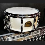 Bílá buben (snare) s chromovanými obručmi a ladicími šrouby. Na korpusu je zlatý oválný štít s nápisem Pearl a pod ním text SIGNATURE SERIES. Buben s…
