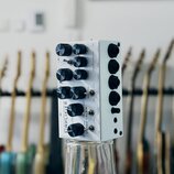 Bílý kytarový zesilovač v kompaktním kovovém boxu s černými ovládacími knoflíky a přepínačem. Na přední straně je svisle napsáno SIMPLIFIER a dále te…