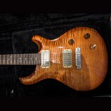 Elektrická kytara s tělem z plamenového javoru v medové barvě. Nástroj má dva humbuckery s krémovými rámečky, jeden bílý přepínač a dva černé oválné…