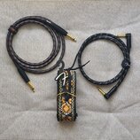 Na fotografii jsou dva instrumentální kabely a jeden kytarový popruh. Levý kabel je šedý s oranžovými proužky a nápisy Roland a RIO-05. Pravý kabel j…