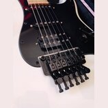 Černá elektrická kytara s černým pickguardem a humbuckerem v pozici u mostu. Nástroj je vybaven černým plovoucím mostem s nápisem Floyd Rose Special.…