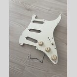 Bílá pickguard pro elektrickou kytaru s třemi výřezy pro snímače. Je na ní osazeno tři ovládací knofíky s nápisy TONE, TONE a VOLUME a jeden přepínač…