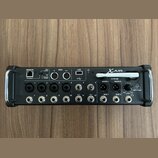 Černý digitální mixér s nápisy XAIR a XR12. Na pravé straně je bílé logo behringer v trojúhelníku. Zařízení obsahuje řadu vstupních konektorů, USB po…